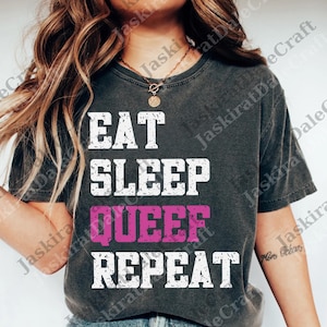 May include: Dark gray t-shirt with the words "EAT SLEEP QUEER REPEAT" in white and pink block letters. The shirt has a crew neck and short sleeves. The text is centered on the front of the shirt.