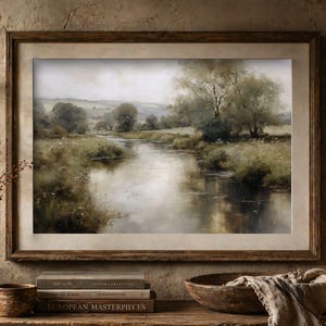 Könnte beinhalten: Ein gerahmtes Landschaftsgemälde zeigt eine ruhige Flussszene mit Bäumen und grasbewachsenen Ufern. Das Kunstwerk befindet sich in einem Holzrahmen, und die Farbpalette ist gedämpft mit Grüntönen, Braun und Grau. Das Gemälde wird auf einer Holzoberfläche ausgestellt.