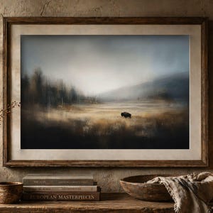 May include: A framed landscape print featuring a solitary bison standing in a vast, golden-brown grassy field under a moody, overcast sky. The scene includes distant dark trees and rolling hills, all rendered in a soft, atmospheric, and painterly style.
