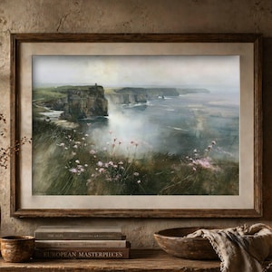 May include: A framed landscape painting depicting a coastal scene with tall cliffs overlooking a calm sea. The foreground features soft pink wildflowers growing on a grassy slope, while the background shows a hazy, overcast sky and distant cliffs.