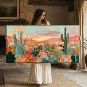 Op de afbeelding: Een groot rechthoekig landschapsschilderij met een woestijnscène met hoge saguaro-cactussen, diverse vetplanten en woestijnflora. Het kleurenpalet bevat tinten blauwgroen, koraal, roze en oranje, die een zonsondergang over heuvels tonen.