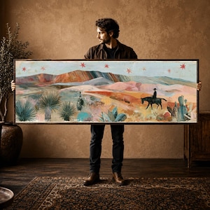 May include: A rectangular landscape painting in a dark wooden frame depicting a desert scene with rolling hills, cacti, and a lone rider on a horse. The sky is filled with red star icons, and the colour palette features muted tones of pink, blue, and tan.