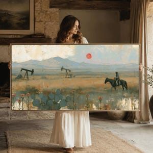 May include: A rectangular landscape painting in a light wood frame depicting a desert scene with oil pumps, a rider on horseback, and prickly pear cacti under a pale sky with a small red sun. The color palette includes muted greens, tans, and blues.
