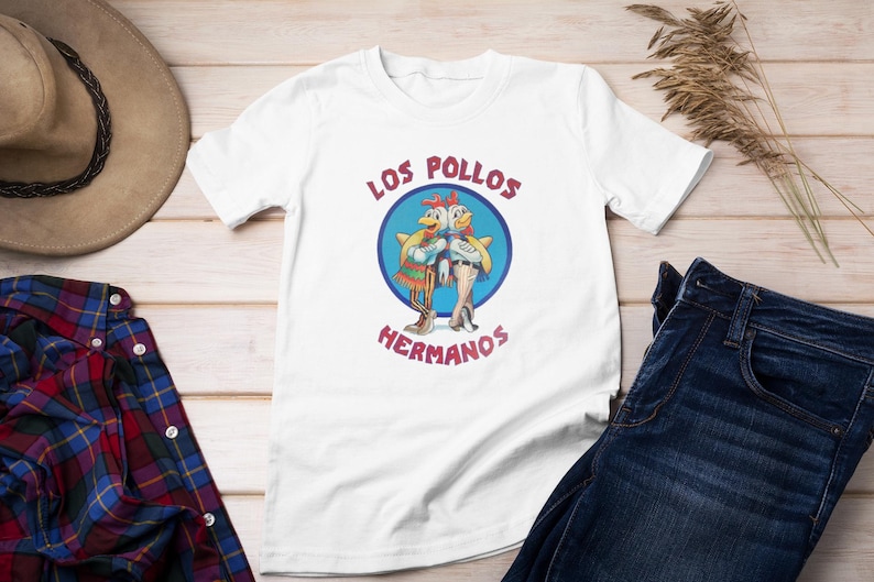 May include: White t-shirt featuring a graphic of two cartoon chickens wearing sombreros and the text "Los Pollos Hermanos".