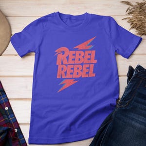 May include: A royal blue t-shirt with a red lightning bolt graphic and the text "Rebel Rebel" printed on the front.