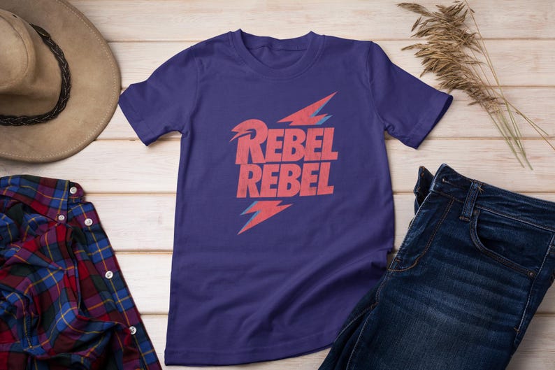 May include: Purple short-sleeved t-shirt with a red lightning bolt graphic and the text "Rebel Rebel" in red.