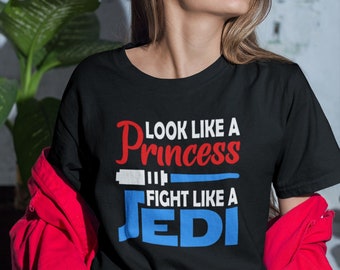 Puede incluir: Camiseta negra con texto blanco que dice "Look like a Princess Fight like a Jedi". El texto está en una fuente estilizada. La camiseta la lleva puesta una persona con el pelo largo y castaño.