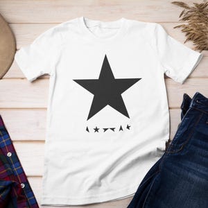 Könnte beinhalten: Weißes T-Shirt mit einem schwarzen Stern und dem Text "A✩✩✩✩✩✩A" auf der Vorderseite.
