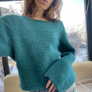 Puede incluir: Suéter de punto color turquesa con cuello ancho y mangas largas. El suéter tiene un aspecto texturizado y un ajuste relajado. Las mangas son ligeramente acampanadas en los puños. El suéter está hecho de un material suave y cálido.