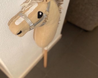 May include: A tan and white stuffed horse head with a silver and black bridle. The horse is attached to a wooden stick.