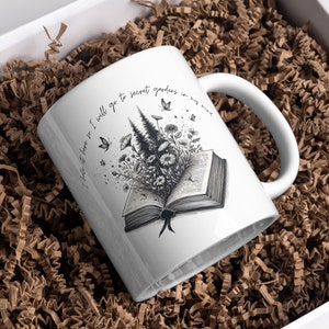 May include: White ceramic mug featuring a black and white illustration of a book with flowers and trees growing out of it. The text on the mug reads "I get lost here for I will go to secret gardens in my mind".