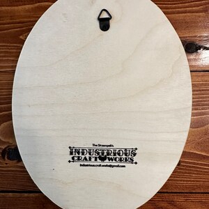 Peut inclure: Dos d'une plaque ovale en bois clair avec un crochet de suspension en m&eacute;tal noir. Le texte "The Strampek's INDUSTRIOUS CRAFT WORKS industrious.craft.works@gmail.com" est imprim&eacute; en noir.