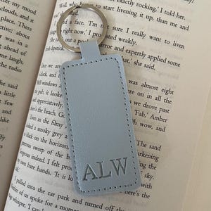 May include: A light blue leather keyring with the initials "ALW" embossed in silver. The keyring is attached to a silver ring.