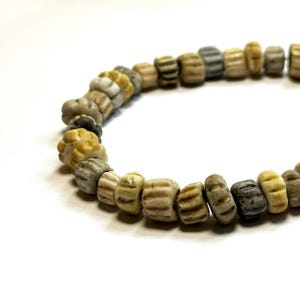 May include: A strand of beige, brown, and grey ceramic beads. The beads are all different shapes and sizes, and some have a textured surface.