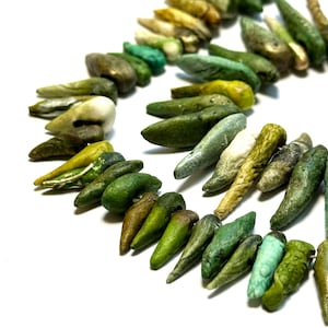 May include: A necklace with a variety of green, yellow, and white elongated beads. The beads have a textured appearance and are arranged in a curved pattern against a white background. The necklace appears to be handmade.