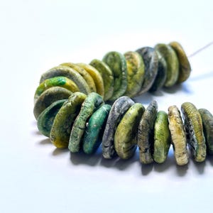 May include: A strand of green, yellow and grey ceramic beads. The beads are round and flat, and they have a textured surface.