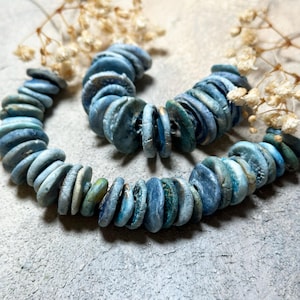 May include: A strand of blue and green ceramic beads with a slightly textured surface. The beads are round and flat, and they are strung together on a clear string.