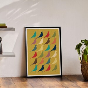 Pode incluir: Uma impressão emoldurada com fundo amarelo apresentando um padrão de pássaros coloridos. Os pássaros estão dispostos em filas e todos estão virados para a mesma direção. A impressão está em uma moldura preta.