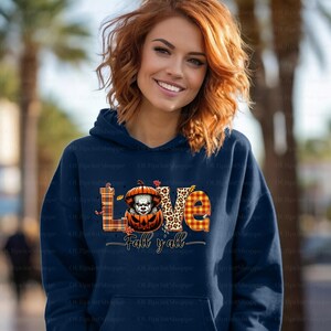 May include: A navy blue hoodie featuring the word "LOVE" in a plaid and leopard print design. A pumpkin with a scary clown face is in the center. The text "Fall y'all" is below the word "LOVE".