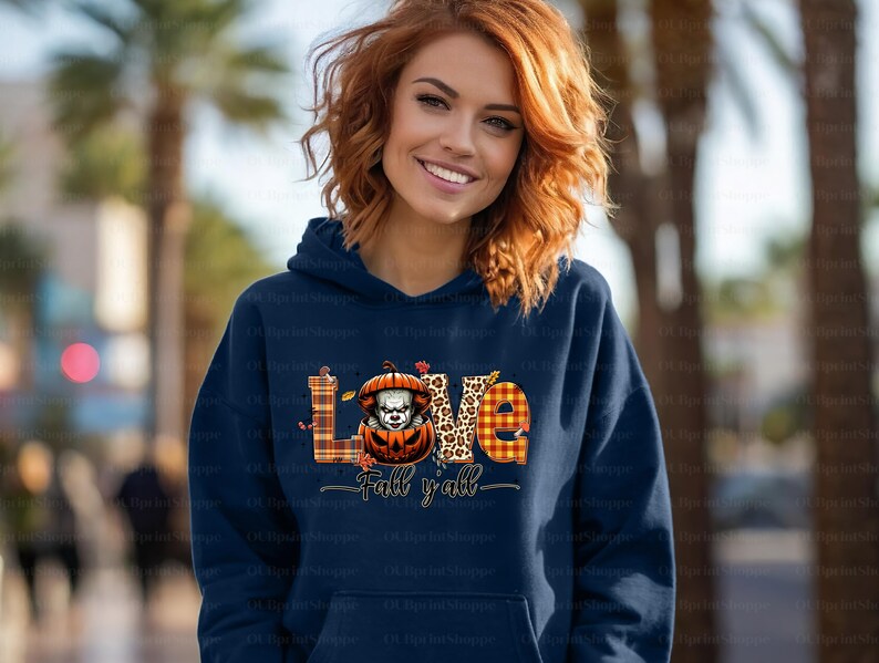 May include: A navy blue hoodie featuring the word "LOVE" in a plaid and leopard print design. A pumpkin with a scary clown face is in the center. The text "Fall y'all" is below the word "LOVE".