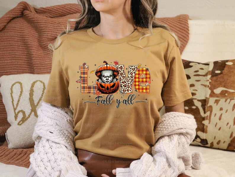 May include: Mustard-coloured t-shirt with a graphic design featuring the word "LOVE" in various patterns, including plaid and leopard print. A pumpkin with a scary face is in the centre. The text "Fall y'all" is below the word "LOVE".