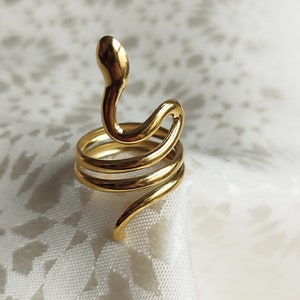 Op de afbeelding: Een gouden slangenring met een gekruld ontwerp. De ring is gemaakt van metaal en heeft een gladde afwerking.
