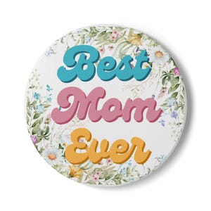 May include: A round white coaster with the words "Best Mom Ever" in teal, pink, and orange, surrounded by a floral design with daisies and other flowers.