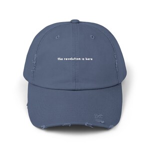 May include: A distressed, dark blue baseball cap with the text "the revolution is here" embroidered in white on the front.