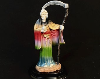 May include: A colorful skeletal figure figurine of the Grim Reaper holding a scythe and a skull. The figure is wearing a long, flowing robe with a rainbow gradient.