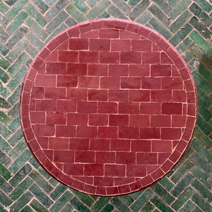 May include: A round table top made of red mosaic tiles. The tiles are arranged in a brick pattern.