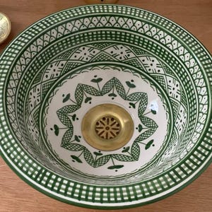 Könnte beinhalten: Ein weißes Keramikwaschbecken mit einem grün-weißen geometrischen Muster. Das Waschbecken ist rund und hat einen Abfluss in der Mitte.