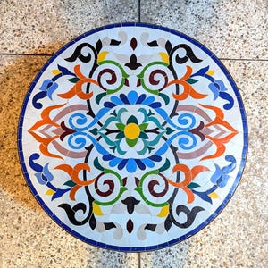 May include: A round table top with a colourful mosaic design. The design features intricate floral patterns in shades of blue, green, orange, red, and yellow. The table top is made of small, square tiles.