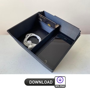 Op de afbeelding: Een zwarte plastic organizer met drie compartimenten. De organizer heeft een creditcard, een paar witte oordopjes en een zwarte smartphone erin.