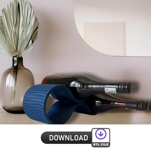 Puede incluir: Un porta botellas de vino de madera azul con dos botellas de vino en su interior. El porta botellas tiene forma de ocho y tiene una textura de grano de madera. Las botellas descansan sobre una superficie blanca.