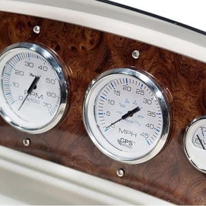 May include: A close-up of a boat's dashboard with four gauges. The gauges are silver with white faces and black needles. The gauges read RPM, MPH, CPS, and VOLTS. The dashboard is made of wood with a brown and white pattern.