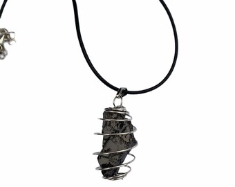May include: A black stone pendant encased in a silver wire cage, hanging from a black cord necklace.