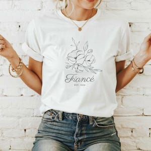 May include: White t-shirt with a floral design and the text "Fiancé Est. 2024".