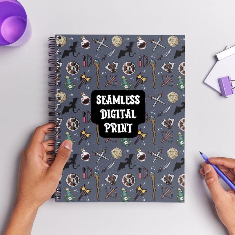 K&ouml;nnte beinhalten: Ein graues Spiralnotizbuch mit einem sich wiederholenden Muster von Fantasy-Symbolen, darunter Drachen, Schwerter, Tr&auml;nke und W&uuml;rfel. Das Notizbuch tr&auml;gt den Text "SEAMLESS DIGITAL PRINT" in Wei&szlig;.
