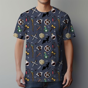 K&ouml;nnte beinhalten: Ein marineblaues T-Shirt mit einem sich wiederholenden Muster aus Fantasy-Rollenspiel-Symbolen. Die Symbole umfassen Schwerter, &Auml;xte, Tr&auml;nke, Schilde, W&uuml;rfel und Drachen.
