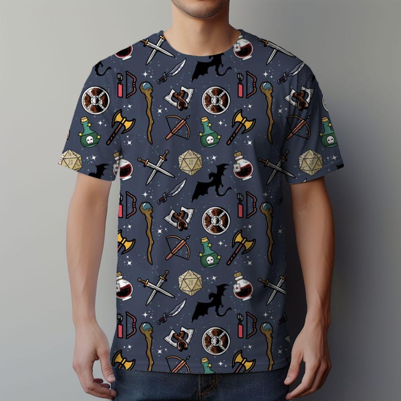 K&ouml;nnte beinhalten: Ein marineblaues T-Shirt mit einem sich wiederholenden Muster aus Fantasy-Rollenspiel-Symbolen. Die Symbole umfassen Schwerter, &Auml;xte, Tr&auml;nke, Schilde, W&uuml;rfel und Drachen.