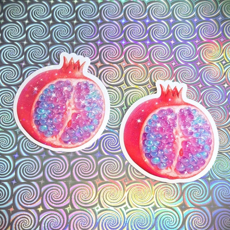 May include: Two pomegranate stickers with a red exterior and a vibrant interior of blue and pink orbs. The stickers are set against a holographic background with a repeating spiral pattern.