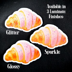 May include: Three croissant stickers with pink icing and glitter details. Available in three finishes: Glitter, Sparkle, and Glossy. The croissants are golden-brown in colour.