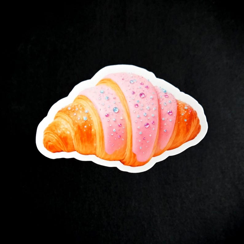 May include: A sticker depicting a croissant with pink icing and sparkling decorations. The pastry is golden brown with a white border, set against a black backdrop. The pink icing is adorned with small, colourful gems.