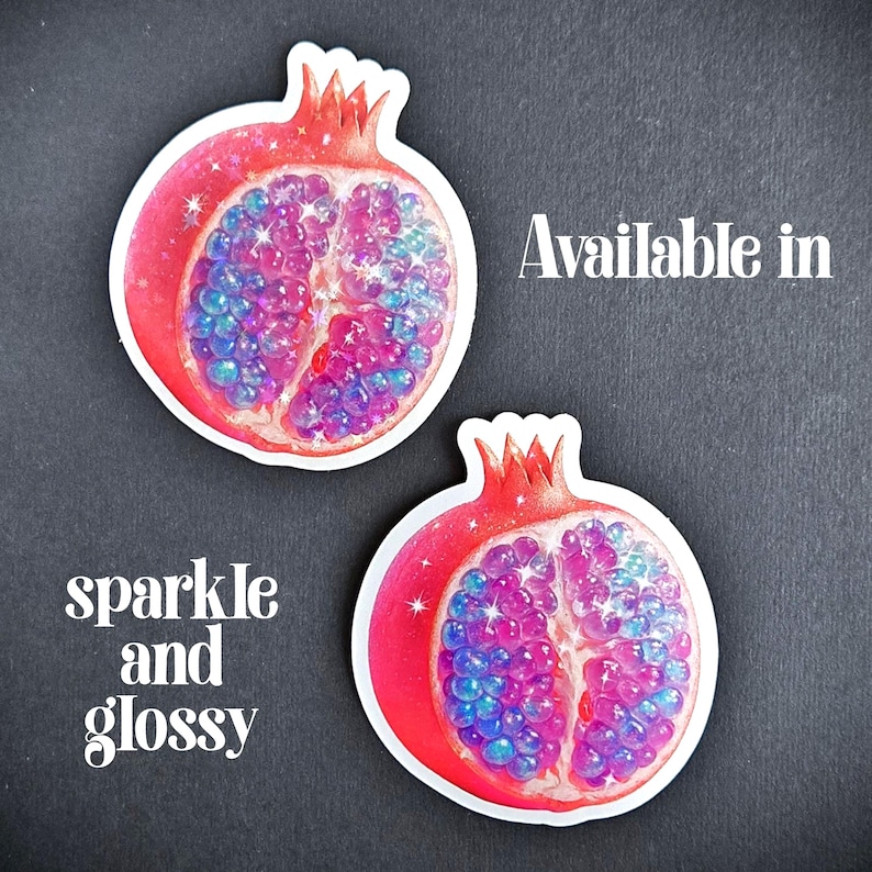 May include: Two glossy, sparkle stickers of a pomegranate cut in half, revealing vibrant pink, purple, and blue seeds. The stickers have a red rind and a white border. Text on the image reads "Available in" and "sparkle and glossy".