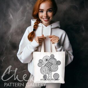 May include: A cream tote bag with a black and white tree design composed of geometric shapes. The bag has a minimalist style, with the words "PATTERN GALLERY" printed on the bottom left.