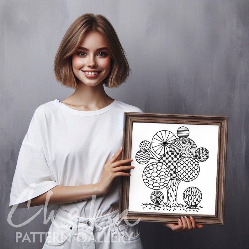 May include: A framed black and white art print depicting a tree with circular, patterned leaves. The artwork is held by a person wearing a white t-shirt and white trousers. The frame is brown.