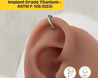 Peut inclure: Un piercing incurvé de couleur argentée avec de petites pierres transparentes est montré dans un perçage d'oreille. Le piercing est étiqueté "Implant Grade Titanium - ASTM F-136 (G23)". La taille de la jauge est de 16 G.