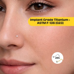 May include: Close-up of a person's face with a nose piercing. The piercing is a small, clear gemstone. The image includes text that reads "Implant Grade Titanium - ASTM F-136 (G23)" and a graphic of a 20G nose ring.