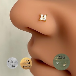 Könnte beinhalten: Ein vergoldeter Nasenpiercing mit einem vierblättrigen Blumenmuster, besetzt mit klaren Edelsteinen. Der Stecker wird an einer Nase gezeigt, mit Details, die darauf hinweisen, dass er 22G ist und aus 925er Silber besteht.