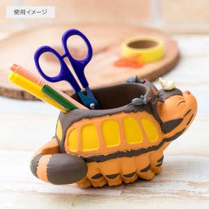 May include: A whimsical orange and yellow bus-shaped desk organizer. The organizer features a cartoon design with a brown interior and is filled with blue scissors, and colorful markers. A small white bird sits on top of the bus.